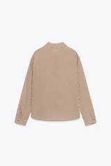 Camisa a rayas verticales marrones y blancas, de corte recto, con cuello solapa y mangas largas con puños abotonados. Presenta bordado floral con abalorios en el frente.