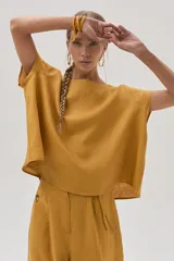 Blusa color mostaza confeccionada en lino, con cuello bote y mangas cortas.
