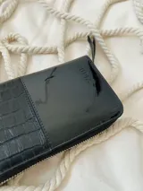 Billetera grande de cuero negro con cierre metálico y logo grabado.