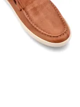 Mocasín de cuero color marrón con cordones decorativos y suela blanca.