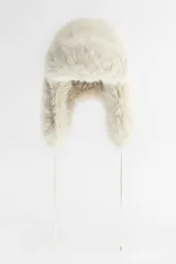 Gorro tipo aviador color crema confeccionado en tejido de pelo sintético. Forro interior combinado a tono. Cierre ajustable con lazada.