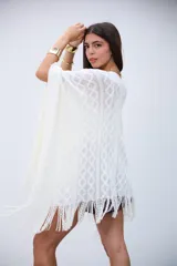 Poncho blanco de tejido calado con diseño geométrico y flecos en el borde.