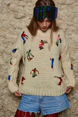 Sweater de lana color crema, tejido a mano con cuello redondo y mangas largas con trenzas. Presenta bordados de figuras esquiando.
