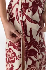 Pantalón largo de tela fluida color beige con estampado de flores grandes color borgoña y abertura lateral en la pierna.