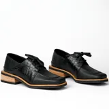 Zapato acordonado de cuero vacuno color marrón oscuro, con suela de goma, horma cuadrada y tacón bajo.