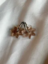 Par de aros colgantes con forma de estrella de seis puntas con glitter color dorado y plateado, con aro de acero quirúrgico.