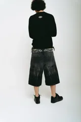 Bermuda de jean negro con lavado ácido gris, corte baggy y bolsillos grandes. Presenta bordados plateados y blancos, cierres y botón personalizado.