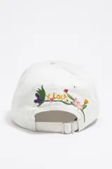 Gorro de béisbol blanco con bordado de flores y logo de la marca Bimba y Lola en amarillo.