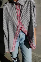 Camisa de poplin negro rayado con corte cómodo, mangas 3/4 y detalles ondeados al frente con zigzag de algodón fucsia y botones fucsia.