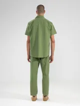 Pantalón de vestir color crema, confeccionado en tejido ligero de algodón con textura seersucker. Tiene corte recto, bolsillos laterales y traseros, cierre con botón y cremallera, y parche con logo de la marca.