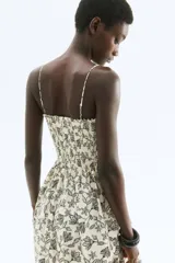 Vestido midi color crudo con estampado de hojas en negro, breteles finos ajustables y escote recto con frunces.