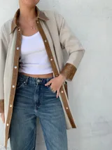 Camisa color beige con detalles en cuero color marrón en cuello, solapa, cierre y puños. Corte recto y abotonada al frente.