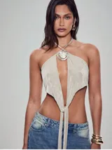 Top halter color beige claro, con escote profundo en V que se anuda en la parte inferior. Presenta un dije metálico con forma de espiral y centro nacarado en el centro del escote.