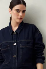 Sobrecamisa oversize de jean azul con cuello camisero, cierre frontal con botones, mangas largas y bolsillos de parche en el pecho.