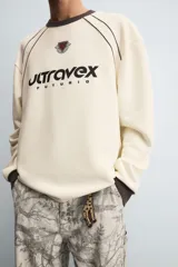 Sudadera color crema de corte relaxed fit, con cuello redondo y manga larga. Presenta un estampado en el frente con la palabra "ULTRAVEX" en letras negras y la palabra "FUTURIO" debajo.