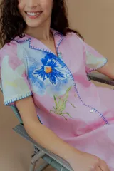 Vestido corto rosado con estampado de flores, cuello solapa, mangas cortas y bordes con puntada overlock en hilo azul.