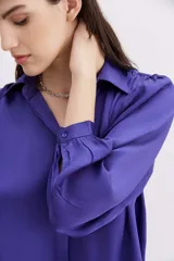 Camisa blanca de manga larga confeccionada en viscosa con acabado sandwash, de textura suave y aterciopelada. Cuello camisero con botón en forma de corazón y frunces en el canesú delantero y la espalda.