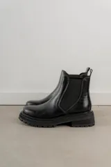 Bota Chelsea de cuero negro con elástico lateral y suela track.