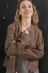 Chaqueta tipo biker de cuero ecológico (PU) color marrón oscuro con efecto desgastado. Presenta cuello mao con broches metálicos, cierre frontal y bolsillos con cremallera.