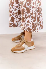 Zapatillas deportivas color beige con detalles metalizados dorados, confeccionadas en cuero con perforaciones, cordones ajustables y suela de goma dentada.