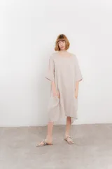 Vestido midi color beige de lino, corte holgado, mangas 3/4 y escote redondo. Presenta bolsillos laterales.
