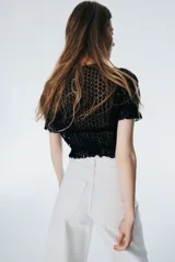 Top corto de punto calado negro con escote redondo, frente abierto con lazos y mangas cortas abullonadas con volados.