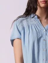 Camisa celeste de tencel con cuello con solapa, escote en V y abertura central con botones. Delantera con detalle en punto smock.
