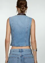 Chaleco de jean celeste con cuello en pico, dos bolsillos delanteros y cierre con botones.