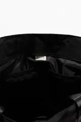 Bolso de deporte negro de tela impermeable con doble asa de mano y correa de hombro ajustable. Tiene bolsillos laterales con cordón elástico y dos compartimentos interiores, uno con cierre y otro de malla.