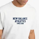Remera gris jaspeado de algodón, con cuello redondo y mangas cortas. Estampado frontal con el texto "New Balance Athletics Since 1906" en azul marino.