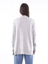 Saco color beige de tejido de punto, con cuello abierto, bolsillos frontales y mangas largas con detalle de botones en los puños.