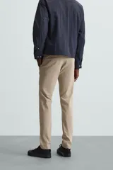 Pantalón chino color beige, corte skinny fit, confeccionado en tejido con mezcla de algodón y elasticidad. Cuenta con bolsillos frontales y traseros. Cierre frontal con cremallera y botón.