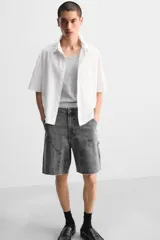 Bermuda color verde militar, de corte relaxed fit, con bolsillos frontales y traseros tipo plaqué, detalle de tira y bolsillo multifunción en la pierna, y bajo irregular.
