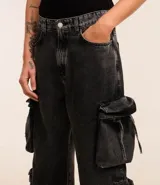 Pantalón de jean super baggy color gris oscuro, con trabillas en la cintura, bolsillos laterales tipo cargo con cordones ajustables y cierre frontal con cremallera y botón.