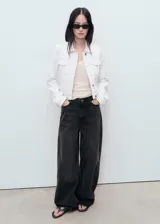 Chaqueta de jean blanca con cuello camisero, bolsillos de parche con solapa en el pecho, cierre frontal con botones y mangas largas con puños abotonados.