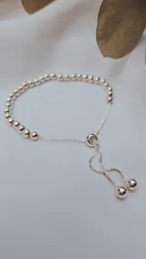 Pulsera ajustable tipo esclava con esferas plateadas lisas y cadena de eslabones finos. Posee un mecanismo de deslizamiento para ajustar el talle y dos esferas colgantes en los extremos de la cadena.