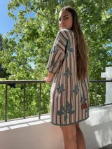 Vestido tejido con hilo de algodón con un diseño de rayas verticales color beige y marrón, con flores color verde agua. Manga corta, cuello redondo y silueta holgada.