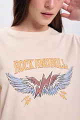Remera color crema de corte cropped, con mangas cortas y estampa frontal con la frase "Rock and Roll" y un rayo alado. 