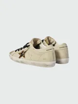 Zapatillas Golden Goose modelo Super Star, color crema con puntera dorada brillante, estrella de animal print y cordones negros.