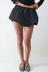 Minifalda negra de tiro bajo con silueta tipo globo, confeccionada en tejido técnico con cintura elástica oculta y bajo redondeado.