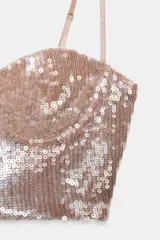 Top corto tipo bralette de escote corazón, cubierto completamente de lentejuelas color oro rosado. Posee tirantes finos ajustables.