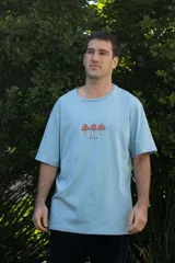 Remera color arena de algodón con cuello redondo y mangas cortas. Estampado frontal con tres hongos rojos y la palabra "Tuya" debajo.