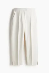 Pantalón cigarette tobillero color blanco, con cintura estándar, cierre y pretina prolongada con corchete oculto. Piernas ajustadas con abertura corta en los bajos, bolsillos al bies y bolsillo de atrás decorativo. Pliegues adelante y atrás.