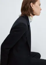 Americana de traje entallada color negro, de manga larga, con solapas con muesca, forro interior, detalle de pinzas, abertura posterior, hombros estructurados y dos bolsillos de ribete en la parte delantera.