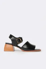 Sandalias negras de cuero con diseño minimalista y taco ancho geométrico en tono madera. La capellada lisa aporta una estética depurada y moderna, mientras que la pulsera con hebilla metálica ajustable asegura un calce firme y confortable.