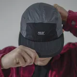 Gorra de cinco paneles con visera plana, color negro con secciones en verde y fucsia.