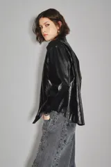 Campera negra de cuero sintético con acabado brillante, cuello camisero, cierre frontal con botones y dos bolsillos delanteros con solapa.