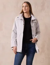 Campera impermeable color gris claro, marca Gallery. Tiene abertura central con cierre oculto y botones a presión, bolsillos delanteros y capucha plegable en el cuello.