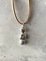 Collar con doble cadena, una tipo choker de cuero negro y otra más larga de cuero color beige, ambas con dije colgante de plata con forma de piedras irregulares.