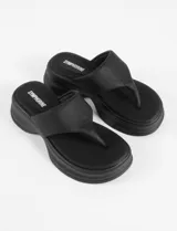 Sandalia negra de plataforma gruesa, estilo ojota o chancla, con tira ancha que sujeta el empeine y separación para el dedo gordo.